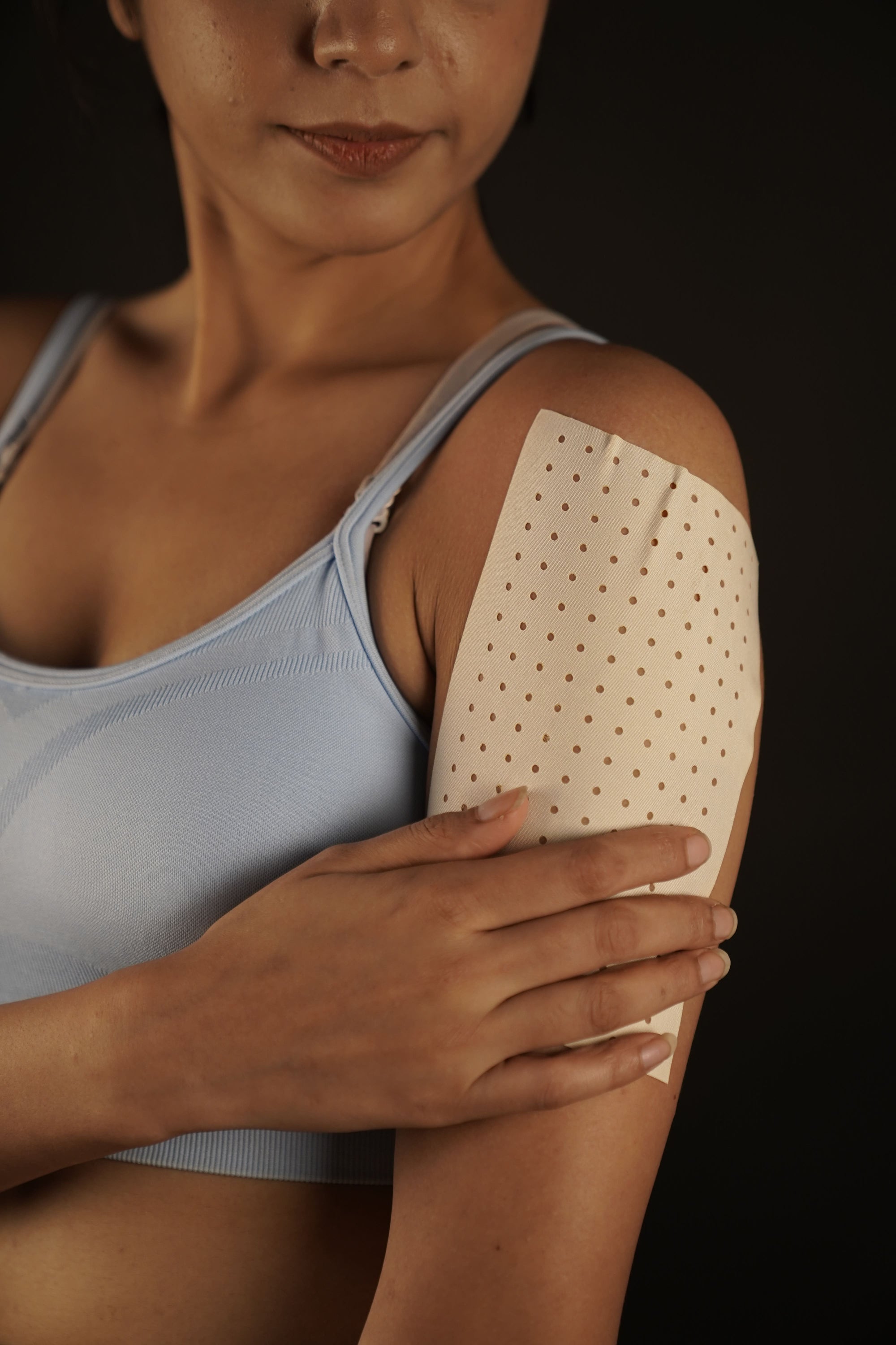 Person applying a adhesive patch on their arm against a dark background